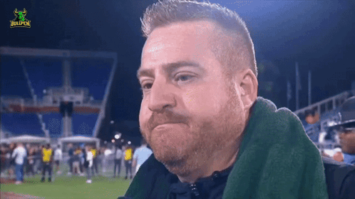 A Man With A Beard Is Sitting In A Stadium With A Bullpen Logo GIF