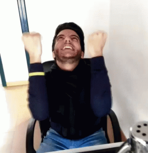A Man With A Beard Is Sitting In An Office Chair With His Arms In The Air GIF