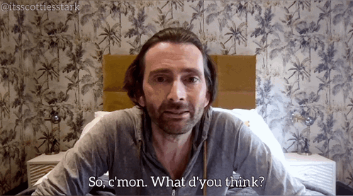A Man With A Beard Is Sitting In Front Of A Bed And Says " So C'mon What D'you Think " GIF