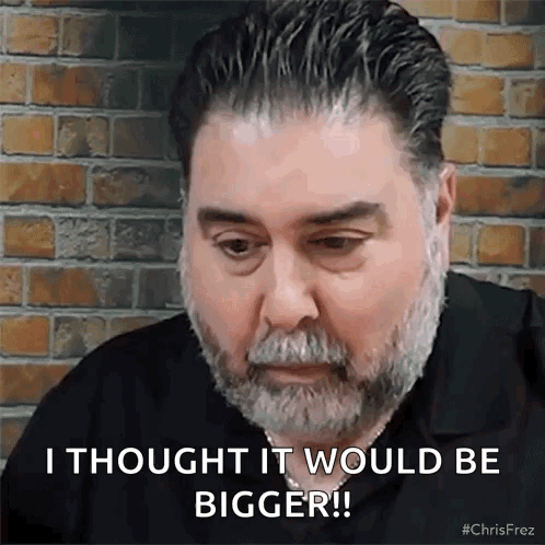 A Man With A Beard Is Sitting In Front Of A Brick Wall . GIF