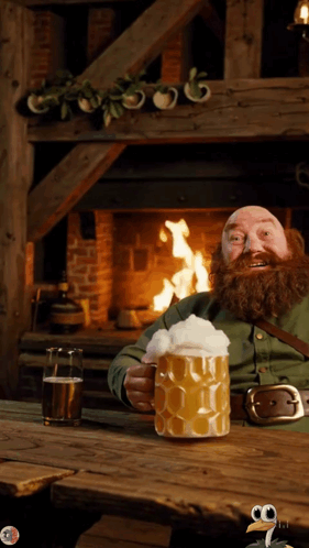 A Man With A Beard Is Sitting In Front Of A Fireplace Holding A Large Mug Of Beer GIF