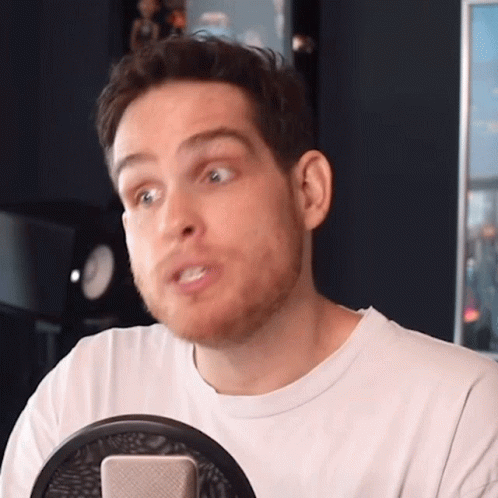 A Man With A Beard Is Sitting In Front Of A Microphone Making A Funny Face GIF