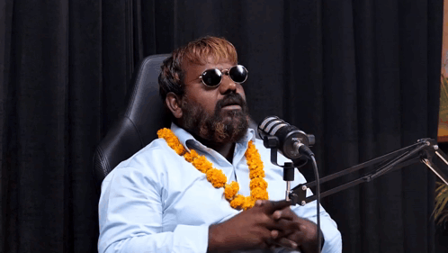 A Man With A Beard Is Sitting In Front Of A Microphone Wearing Sunglasses GIF
