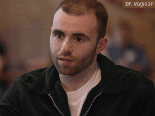 A Man With A Beard Is Sitting In Front Of A Sign That Says Dr. Vagin GIF