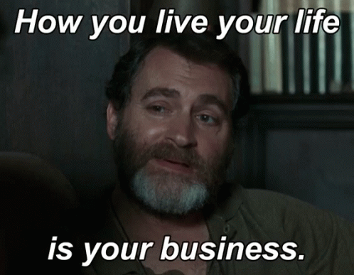 a man with a beard is sitting in front of a sign that says " how you live your life is your business "