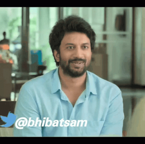 A Man With A Beard Is Sitting In Front Of A Twitter Logo That Says @Bhibatsam GIF
