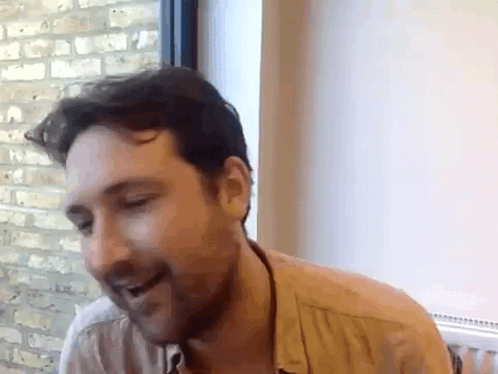 A Man With A Beard Is Sitting In Front Of A Window . GIF
