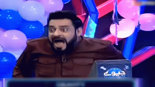 A Man With A Beard Is Sitting In Front Of Balloons And A Sign That Says " Jio " GIF