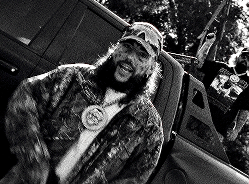 A Man With A Beard Is Sitting In The Back Of A Truck With A Gun . GIF