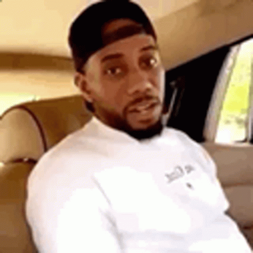 A Man With A Beard Is Sitting In The Back Seat Of A Car Wearing A Hat And A White Shirt . GIF