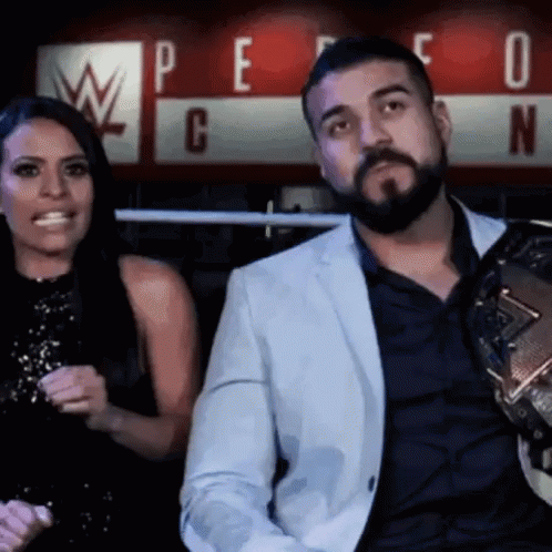 A Man With A Beard Is Sitting Next To A Woman In Front Of A Sign That Says W GIF