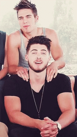 A Man With A Beard Is Sitting Next To Another Man With His Hands On His Shoulders GIF