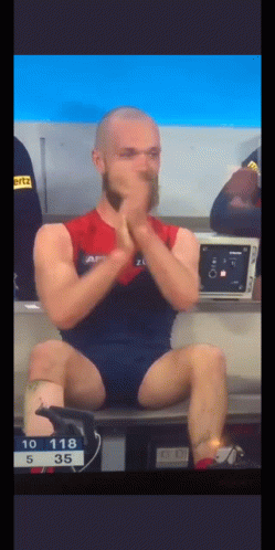 A Man With A Beard Is Sitting On A Bench With His Legs Crossed And His Hands On His Face . GIF