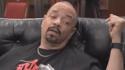 a man with a beard is sitting on a black leather couch making a funny face .