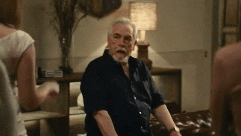 A Man With A Beard Is Sitting On A Couch In A Dark Room GIF