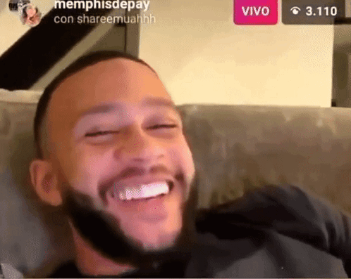 a man with a beard is sitting on a couch smiling