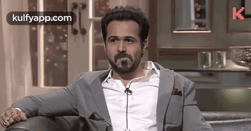 A Man With A Beard Is Sitting On A Couch Wearing A Suit And Tie . GIF