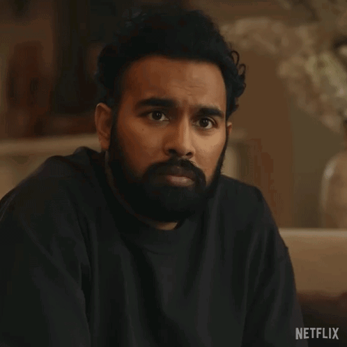 A Man With A Beard Is Sitting On A Couch With His Eyes Closed And A Black Shirt On . GIF