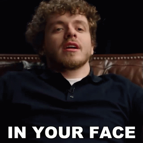 A Man With A Beard Is Sitting On A Couch With The Words In Your Face Behind Him GIF
