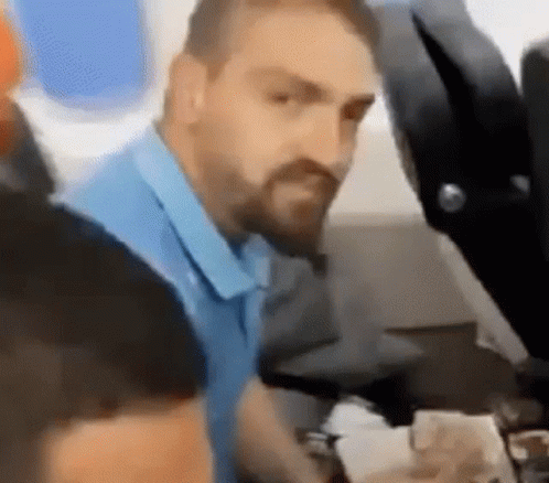 A Man With A Beard Is Sitting On A Plane Looking At Something . GIF