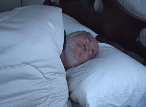 A Man With A Beard Is Sleeping In A Bed GIF