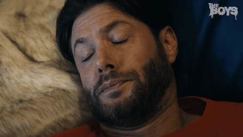 A Man With A Beard Is Sleeping In A Bed With The Boys Written In The Background GIF