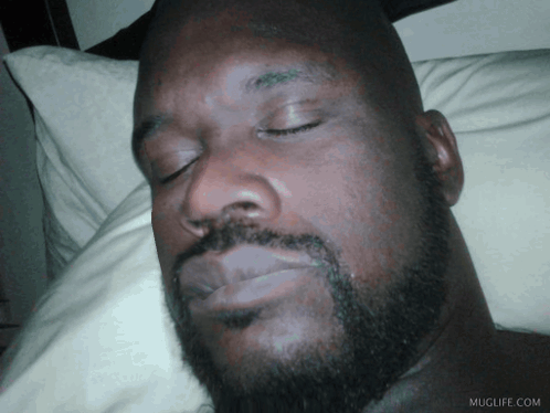 A Man With A Beard Is Sleeping On A Bed With Muglife.com Written On The Bottom Right GIF