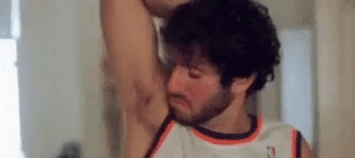 A Man With A Beard Is Smelling His Armpit In A Room . GIF