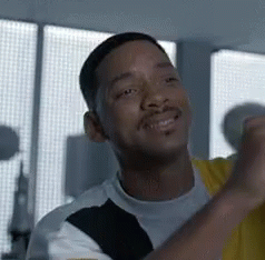 A Man With A Beard Is Smiling And Looking At The Camera While Standing In Front Of A Window . GIF