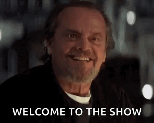 A Man With A Beard Is Smiling And Saying Welcome To The Show GIF
