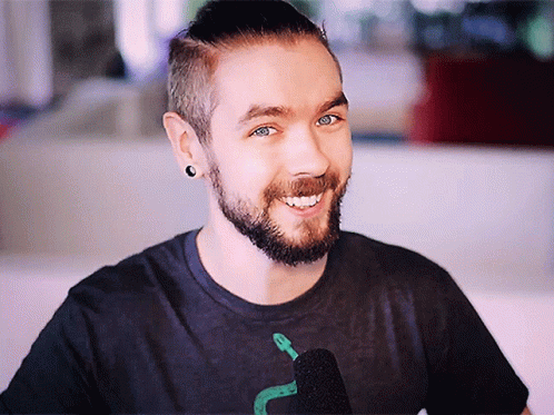 A Man With A Beard Is Smiling And Wearing A Black Shirt With A Snake On It GIF