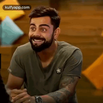 A Man With A Beard Is Smiling And Wearing A Watch While Sitting Down . GIF