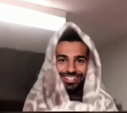 A Man With A Beard Is Smiling And Wrapped In A Blanket . GIF