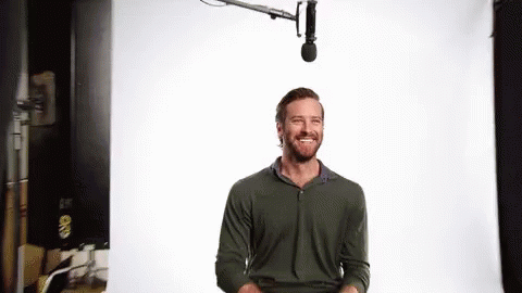 A Man With A Beard Is Smiling In Front Of A Microphone In A Studio . GIF