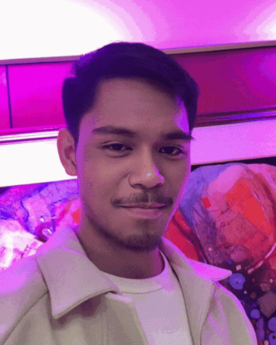 A Man With A Beard Is Smiling In Front Of A Painting GIF