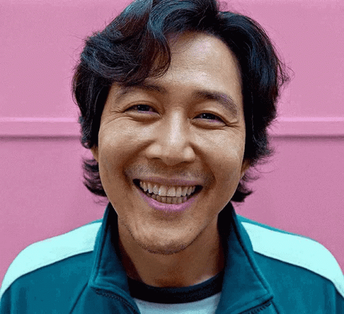 A Man With A Beard Is Smiling In Front Of A Pink Wall . GIF