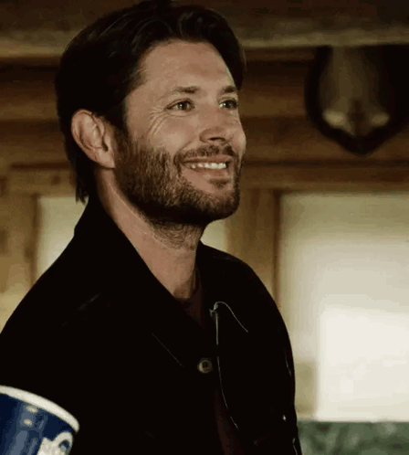 A Man With A Beard Is Smiling While Holding A Cup Of Coffee . GIF