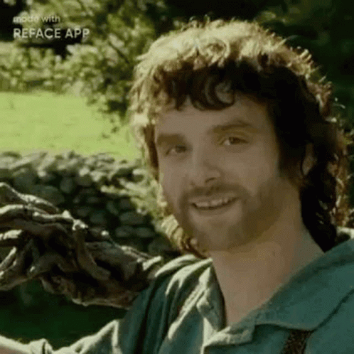 A Man With A Beard Is Smiling While Holding A Tree Branch In His Hands . GIF