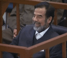 A Man With A Beard Is Smiling While Sitting Behind A Wooden Fence GIF
