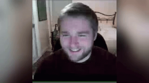 A Man With A Beard Is Smiling While Sitting In Front Of A Computer Monitor . GIF