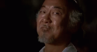 A Man With A Beard Is Smiling With His Eyes Closed While Sitting In A Dark Room . GIF