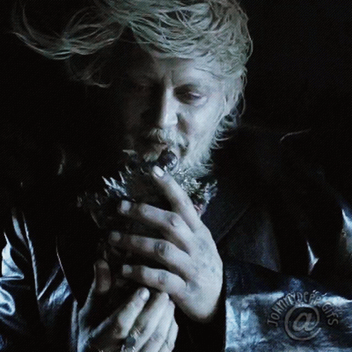 A Man With A Beard Is Smoking A Cigarette In A Dark Room With Tommy Doe 'S Logo On The Bottom Right GIF