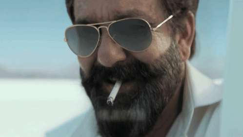 A Man With A Beard Is Smoking A Cigarette GIF