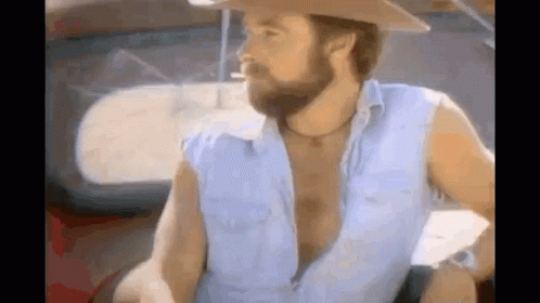 A Man With A Beard Is Smoking A Cigarette While Wearing A Cowboy Hat . GIF