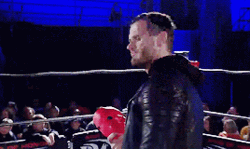 A Man With A Beard Is Speaking Into A Microphone In Front Of A Crowd Of People GIF
