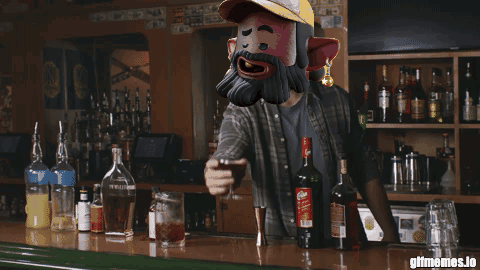 A Man With A Beard Is Standing At A Bar Holding A Glass GIF