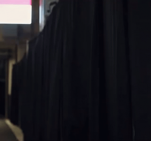 A Man With A Beard Is Standing Behind A Black Curtain In A Room . GIF