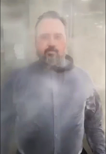 A Man With A Beard Is Standing Behind A Clear Glass GIF