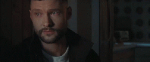 A Man With A Beard Is Standing In A Dark Room Looking At Something . GIF