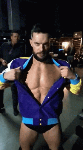 A Man With A Beard Is Standing In A Dark Room Taking Off His Shirt GIF